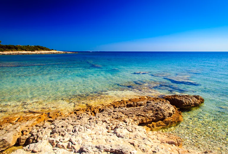 Sandy turquoise bay near Pula with anchored boats and shallow swimming water
