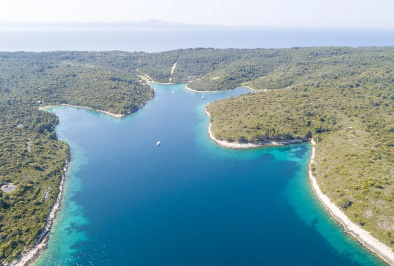 Aerial of a long sheltered island inlet with only a few sailboats anchored in clear water
