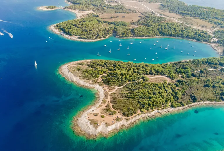 Aerial of Cape Kamenjak coves with anchored sailboats in turquoise bays
