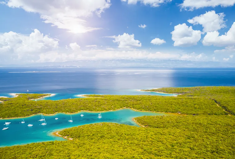 Aerial of forested island bays with anchored sailboats in bright sun
