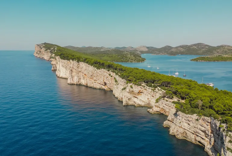 Aerial of long limestone sea cliffs with sailboats anchored beyond