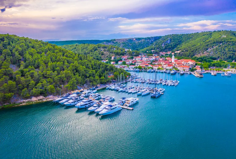 Aerial of Skradin riverside marina with moored yachts below a hilltop village at dusk
