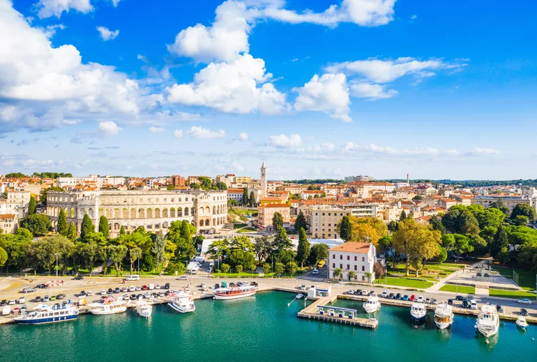 Aerial of the Pula Roman amphitheatre, city skyline and boat-lined harbourfront