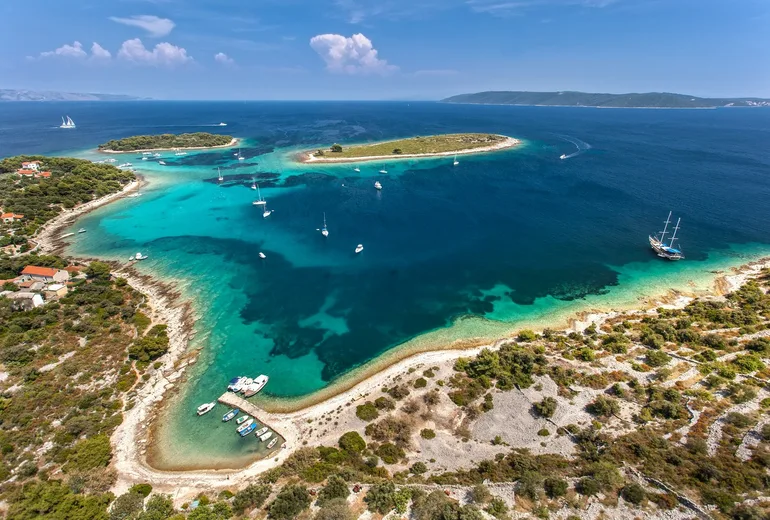 Aerial of the turquoise Krknjaši Blue Lagoon at Drvenik Veli with anchored sailboats and a gulet