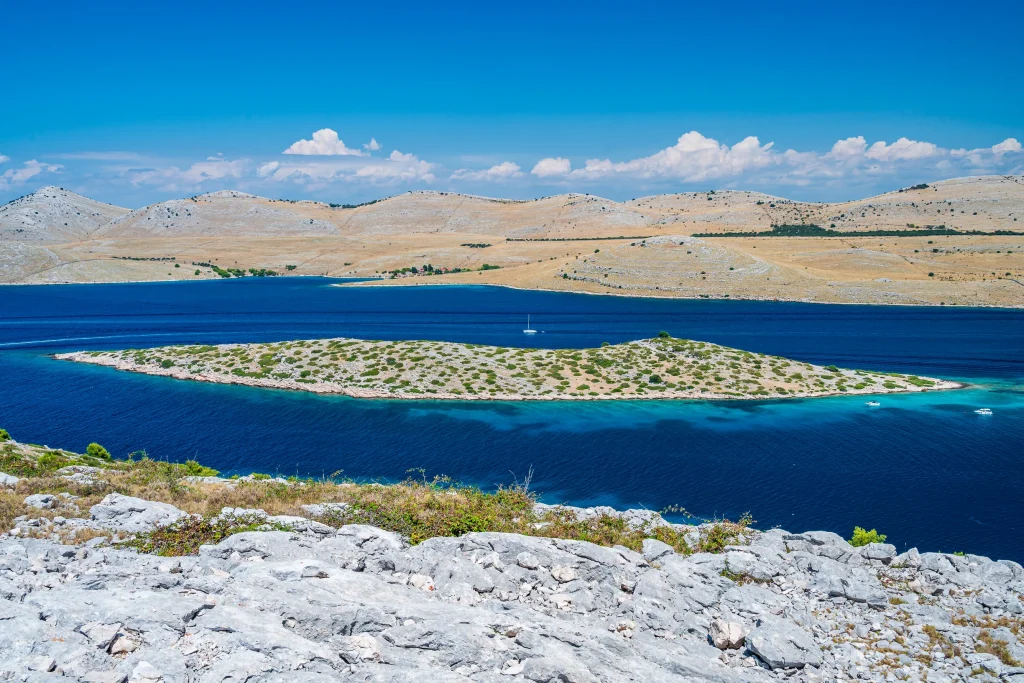 Barren Kornati island hills and walled islet viewed from rocky ridge over blue sea