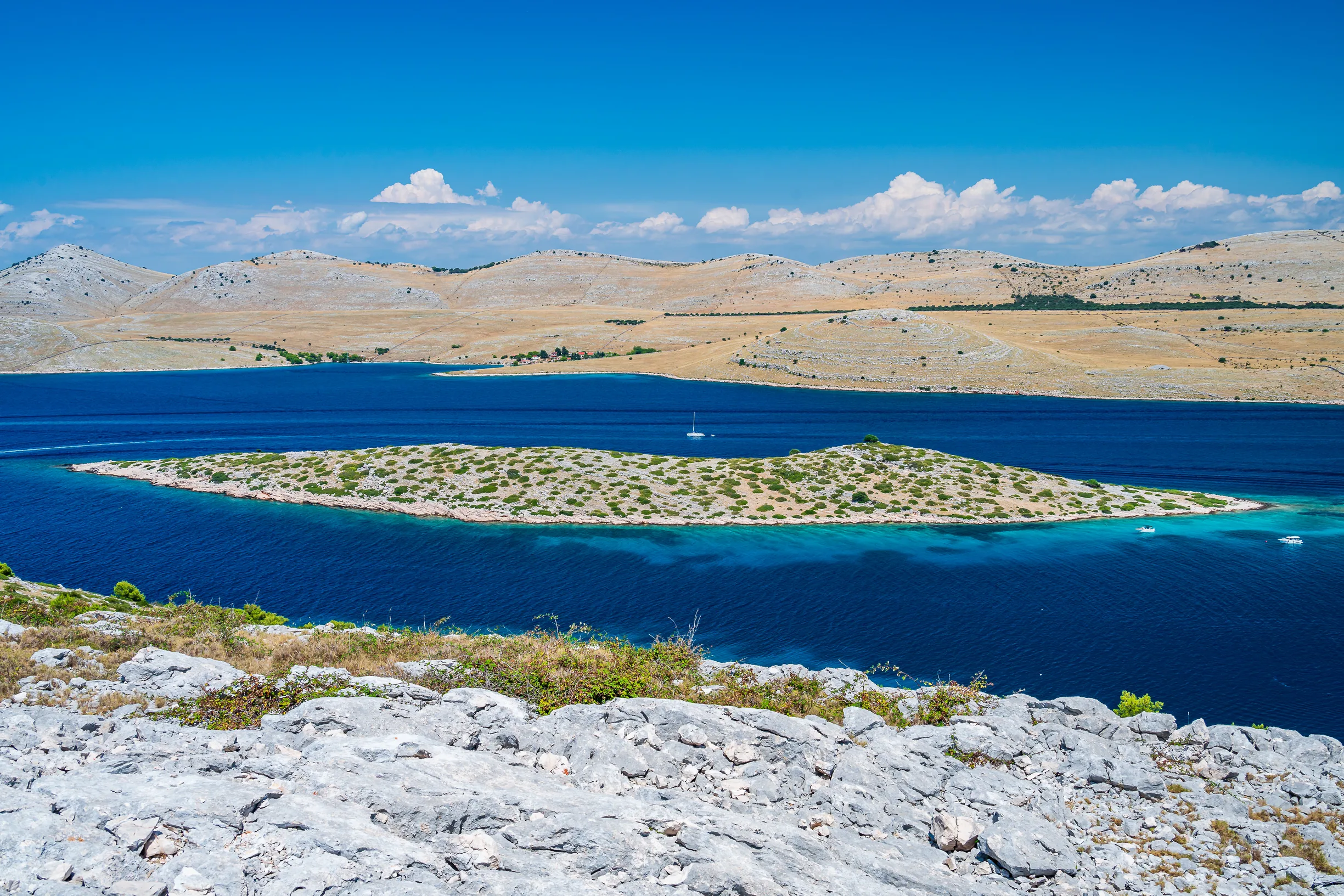 Barren Kornati island hills and walled islet viewed from rocky ridge over blue sea