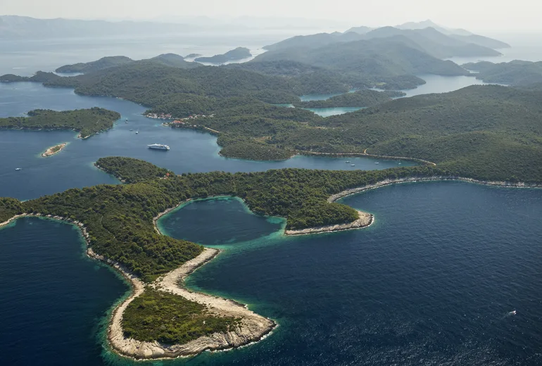 Hazy aerial of a densely forested island coastline with deep sheltered coves