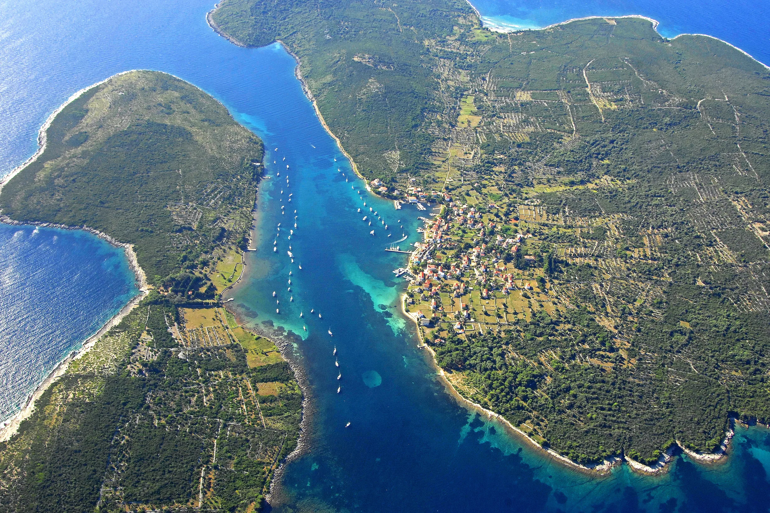 Aerial of narrow channel between green islands with village and moored yachts