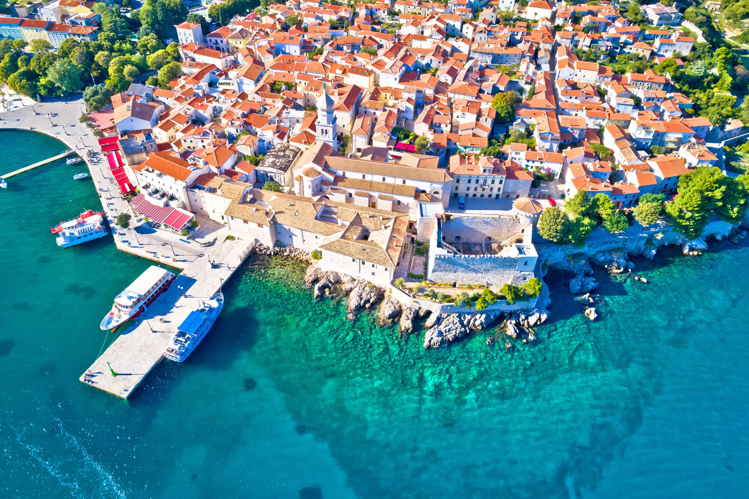 Aerial of Krk old town rooftops, bell towers and piers over turquoise sea