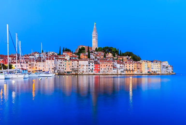 Rovinj old town and moored sailboats reflected in calm sea at blue hour
