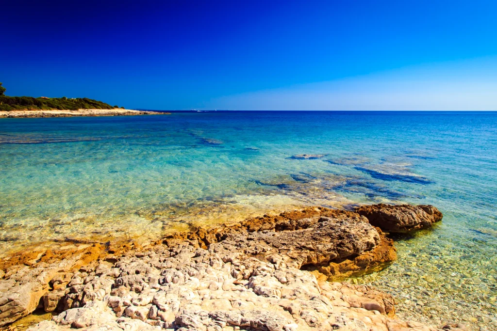 Rocky Valbandon shoreline in Istria with clear turquoise shallows under deep blue sky