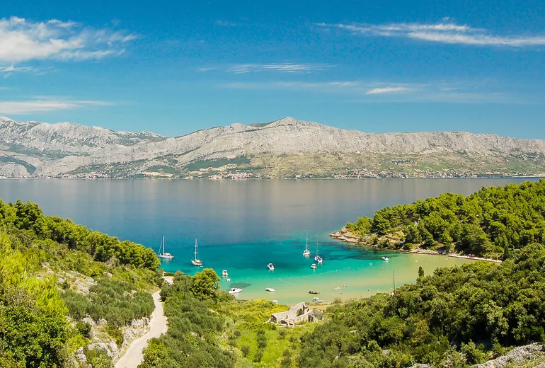 Sandy cove with anchored sailboats below bare coastal mountains