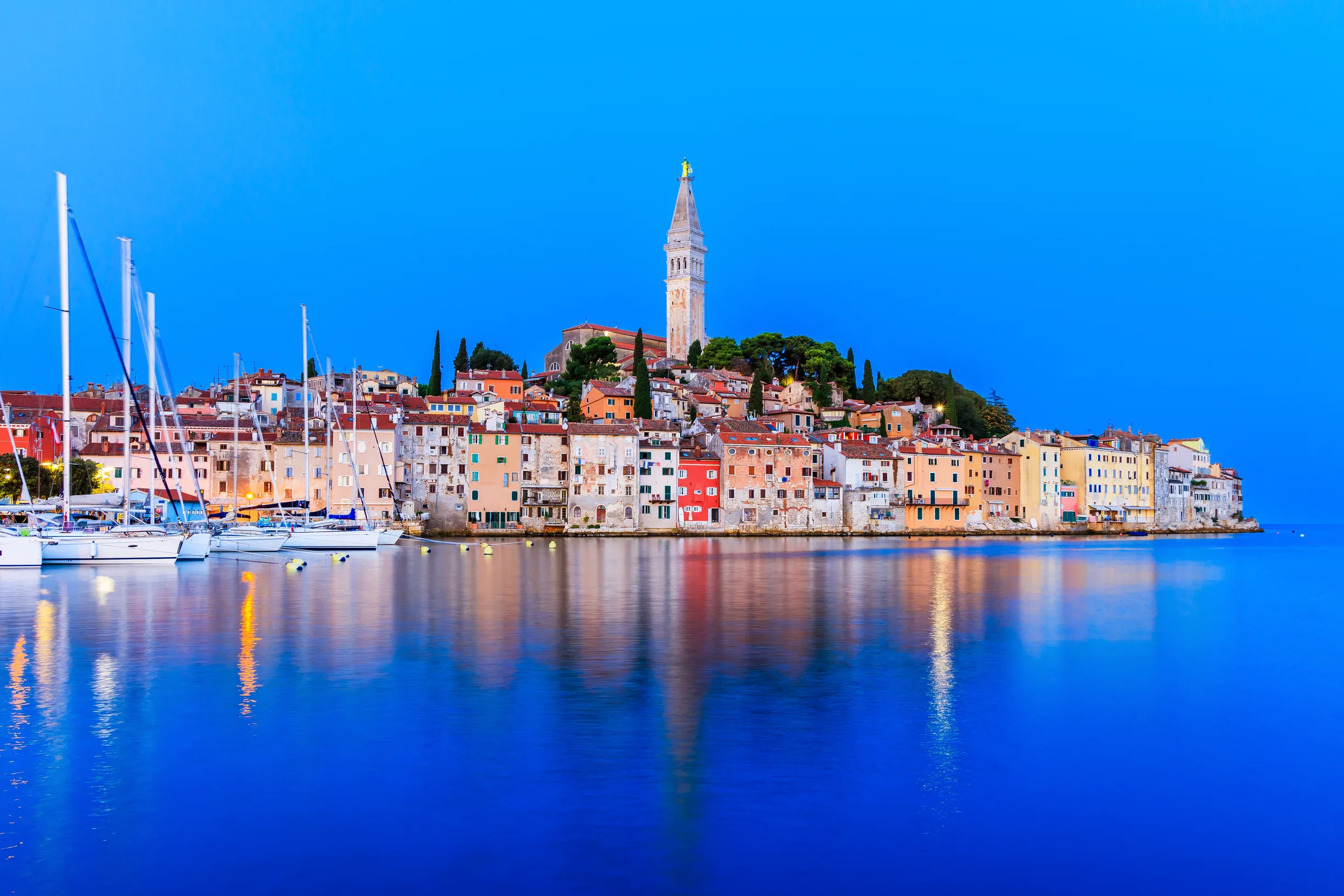 Rovinj old town and moored sailboats reflected in calm sea at blue hour