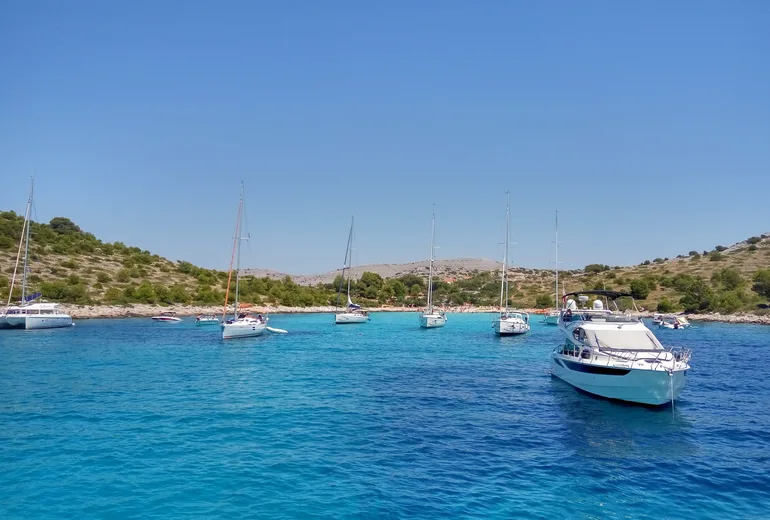 Yachts moored in a turquoise Kornati cove with barren hills and a small beach